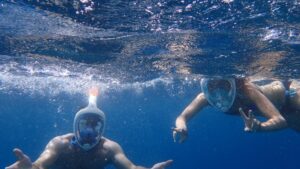 Two snorkelers underwater, wearing full-face snorkel masks and swimming in clear blue water