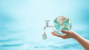 A close-up of a hand holding a water globe with a faucet dripping a single drop of water. The globe is a representation of Earth